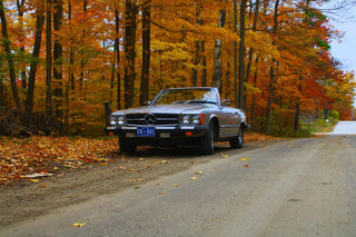 Classic Mercedes-Benz R107 SL convertible parked on a country road surrounded by autumn trees