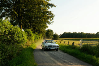 Classic Mercedes-Benz SL convertible being driven along a rural gravel lane